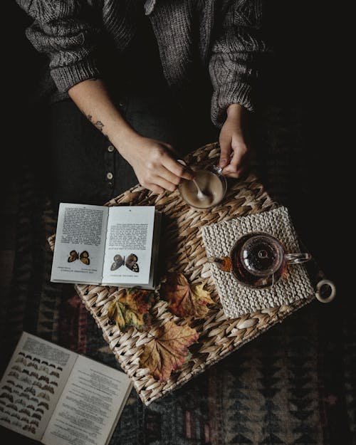 Free From above of crop faceless person holding cup of fresh coffee while sitting at table and reading book about butterflies Stock Photo