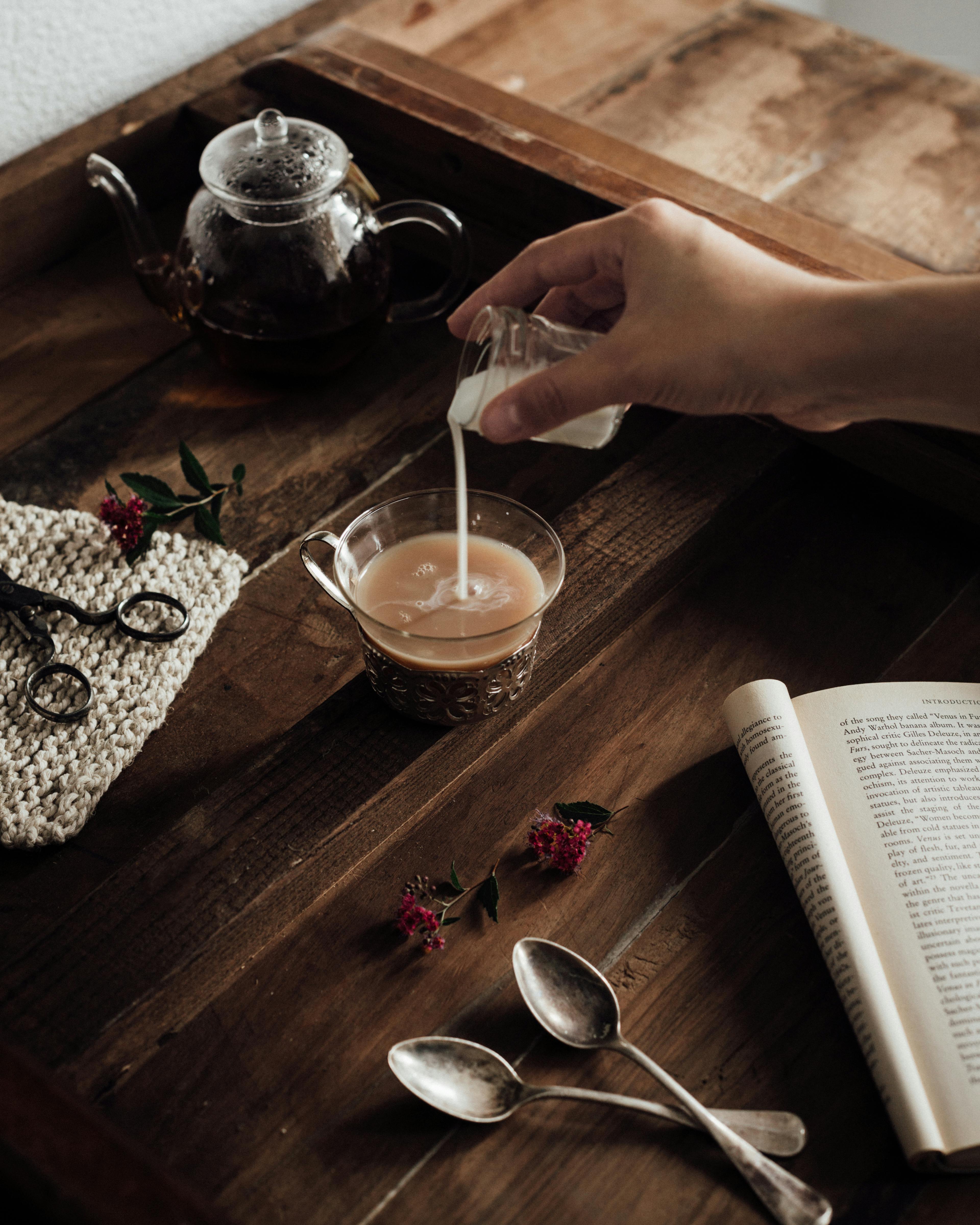 crop person pouring milk in cup of coffee