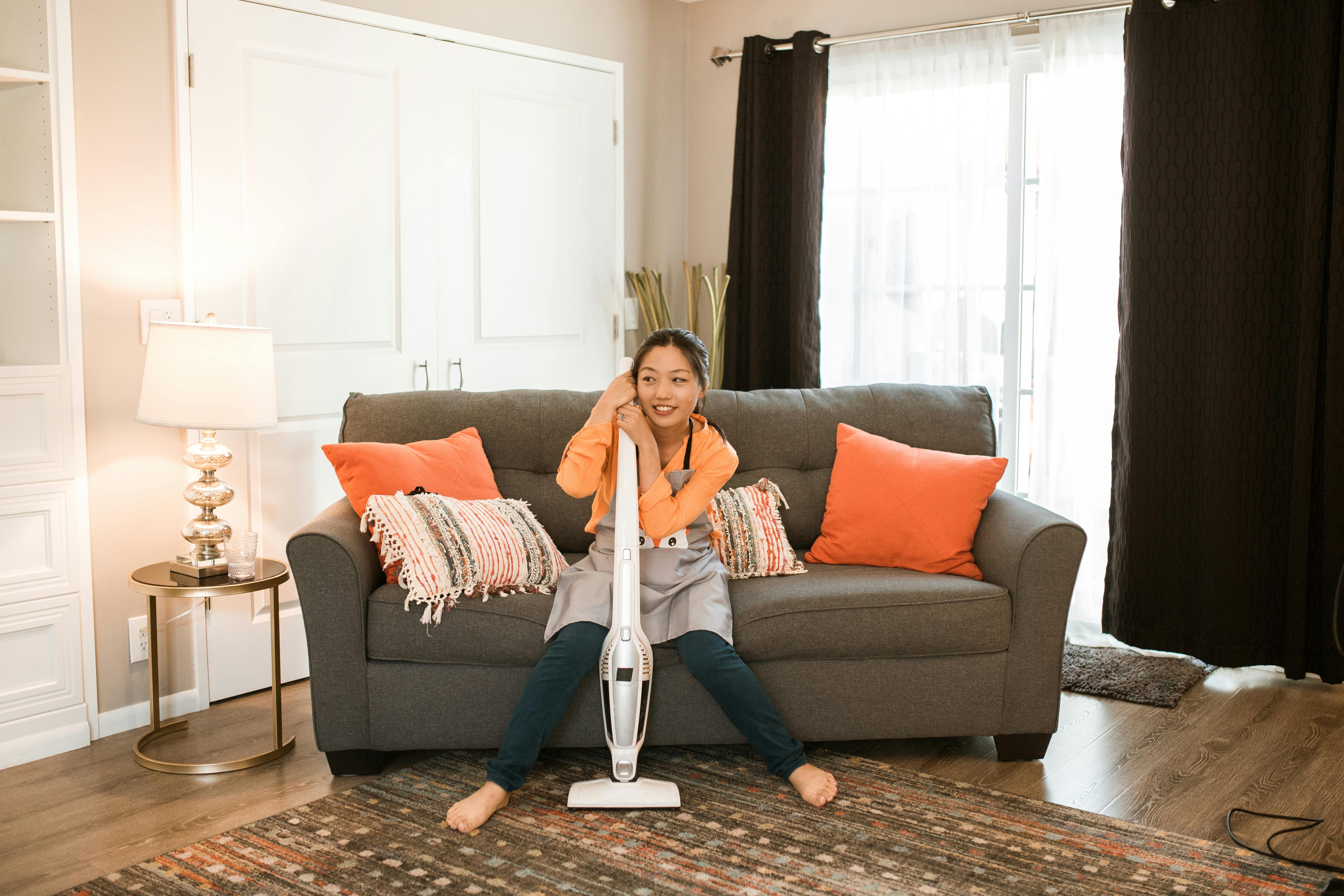 Woman in apron sitting on couch with vacuum cleaner in stylish living room.