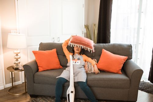 Free Young girl playing with pillows on a cozy couch indoors, surrounded by warm decor. Stock Photo