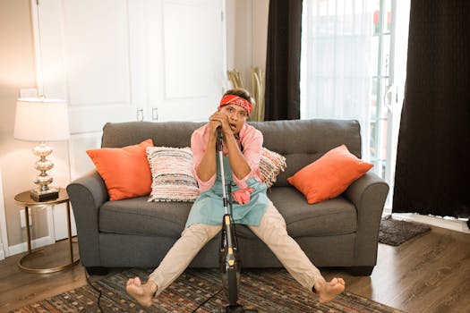 Relaxed man resting on sofa at home with vacuum cleaner, capturing a moment of exhaustion after chores.