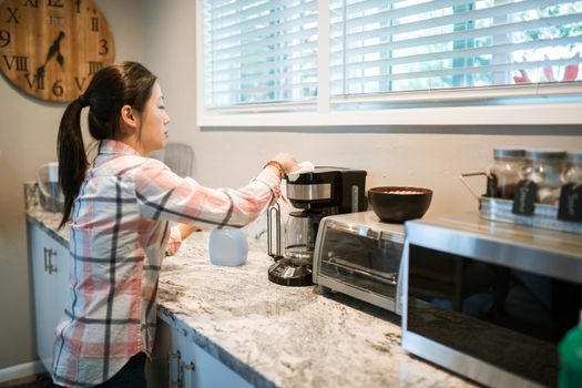 Woman cleaning a coffee maker in a bright, modern kitchen with appliances.