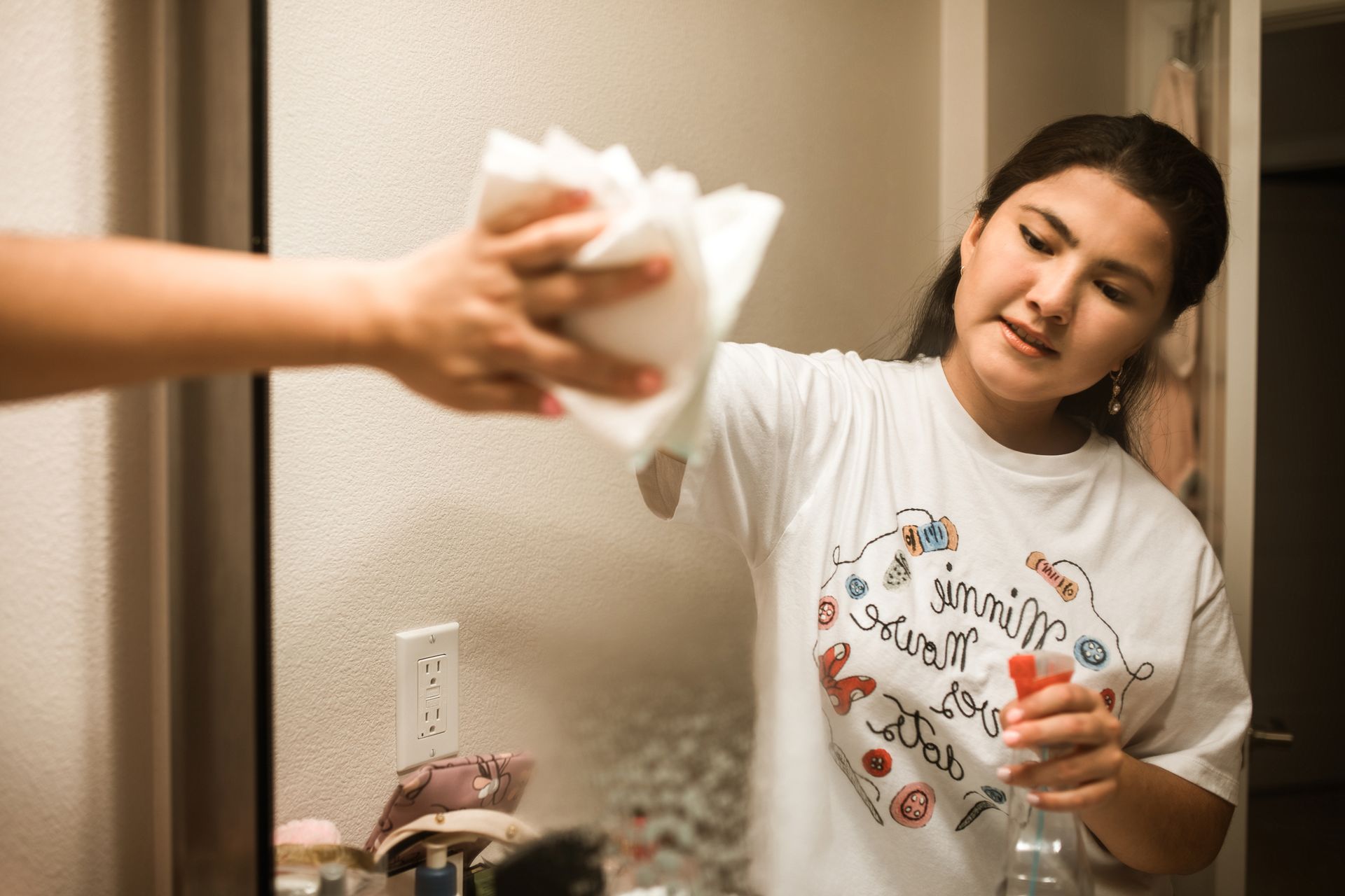 Woman cleans bathroom mirror with spray in relaxing home setting.