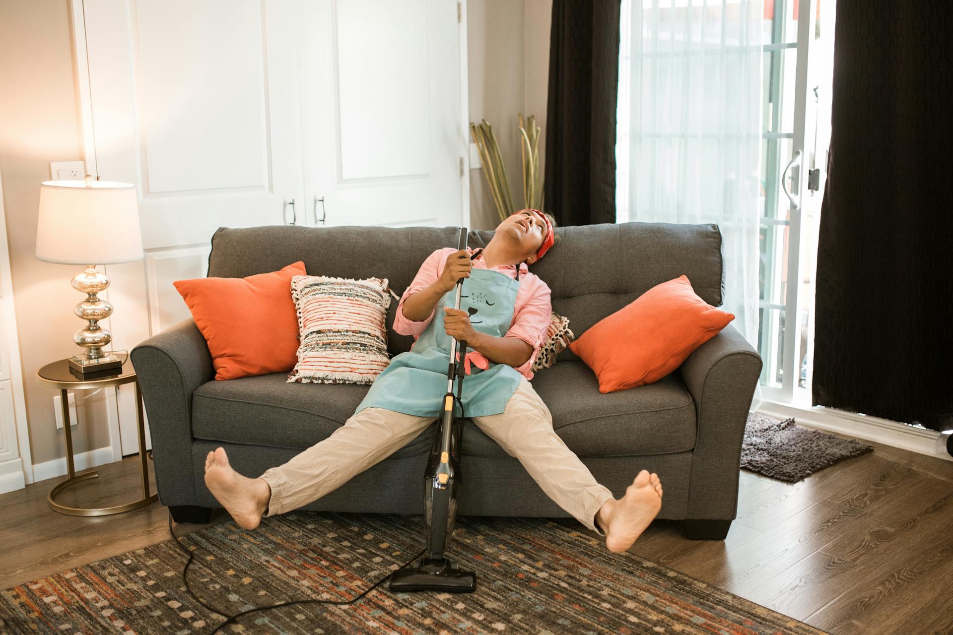 Man exhausted after vacuuming, resting on a couch with a vacuum cleaner at home.