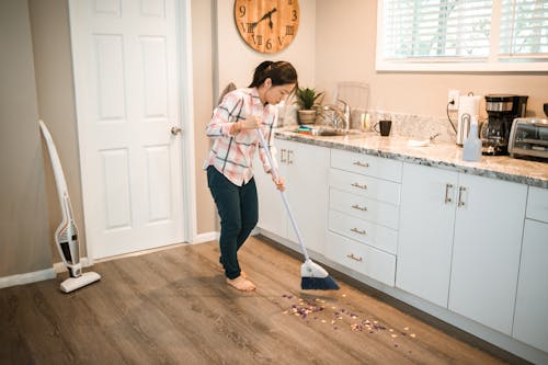 Free Photograph of a Woman in a Plaid Shirt Sweeping with a White Broom Stock Photo