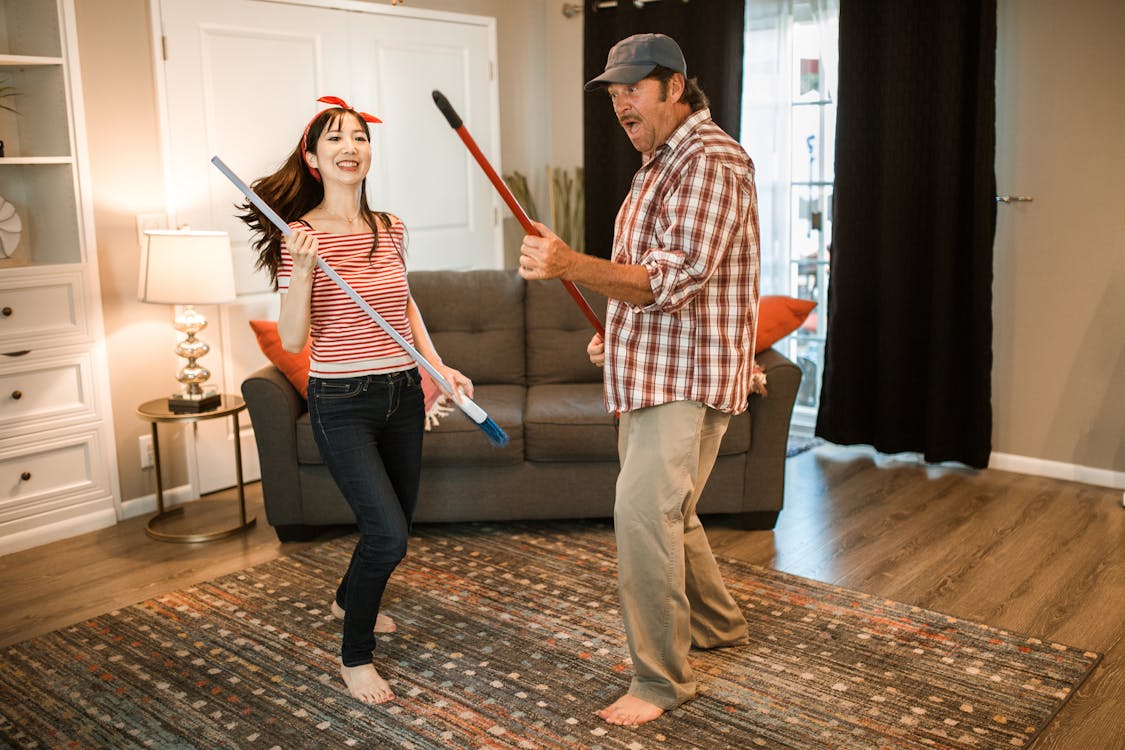 Photo of a Man and a Woman Using Brooms as Guitars