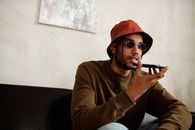 一位时尚的年轻人戴着太阳镜和水桶帽，在室内用智能手机打着语音电话