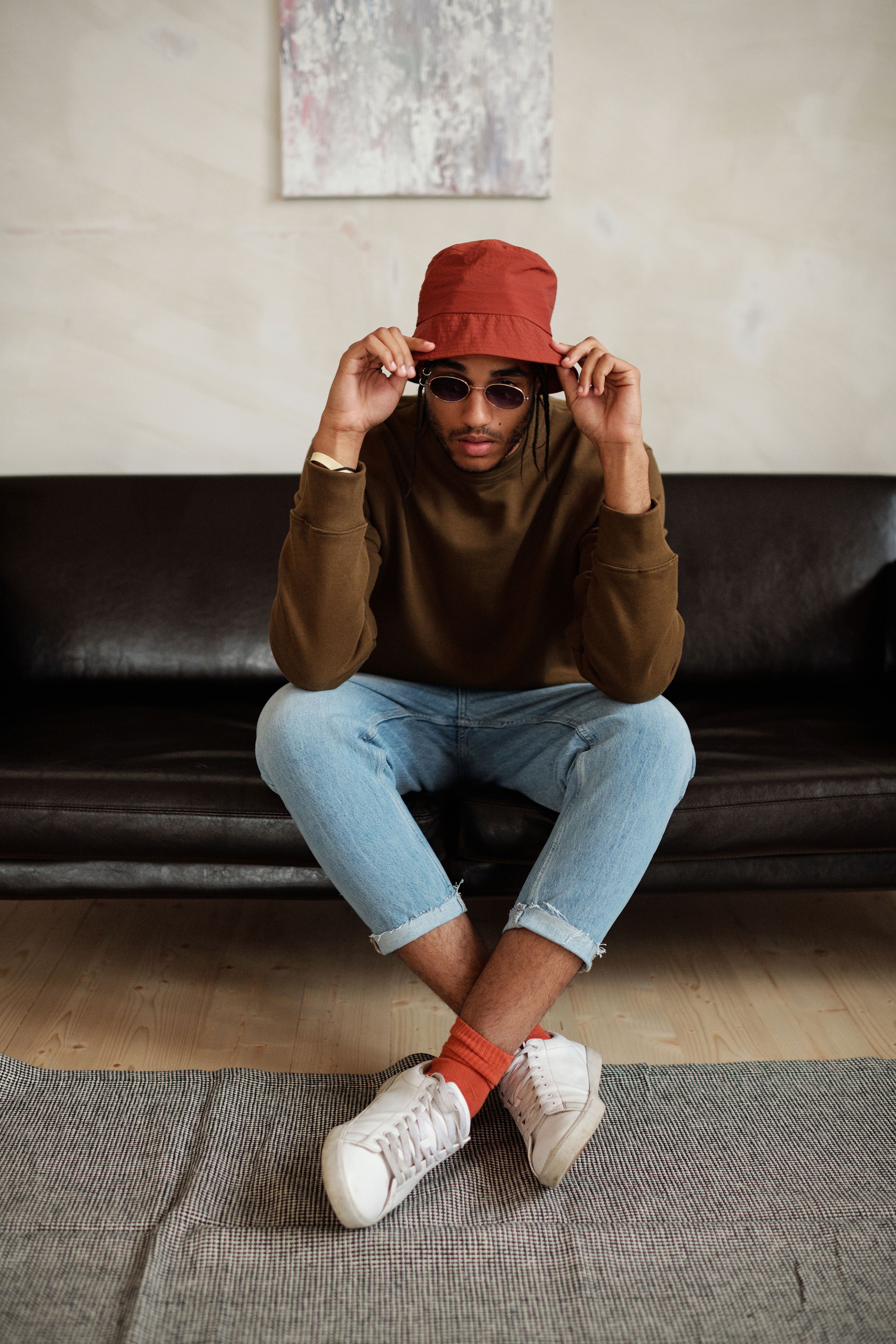 Um jovem fashionista sentado em um sofá de couro, vestindo streetwear com óculos de sol e chapéu bucket.