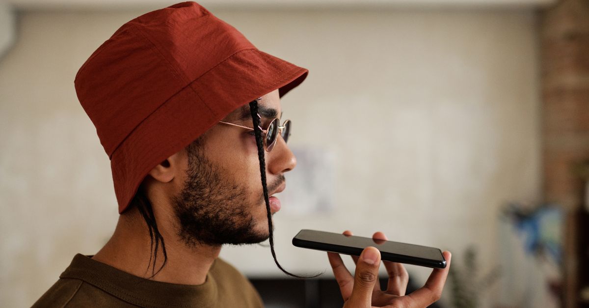 Vista de perfil de um homem com um chapéu bucket vermelho falando ao smartphone dentro de casa.