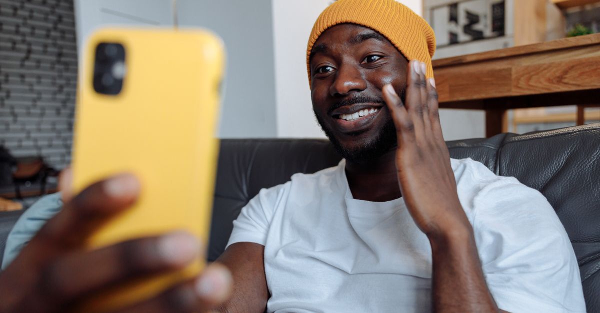 Um homem alegre em um gorro fazendo uma chamada de vídeo em seu smartphone dentro de casa.