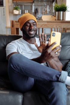African American man wearing a beanie having a friendly video call on smartphone while sitting indoors.