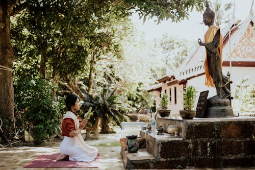 A Woman Kneeling Near a Buddha Statue