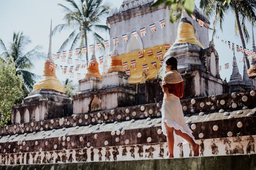 A woman in traditional attire walking near a decorated Buddhist temple with vibrant flags.