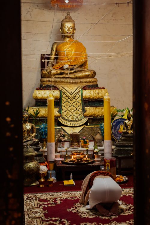 Free A person kneeling in prayer at a Buddhist shrine with a golden statue. Stock Photo
