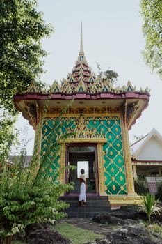 一名妇女站在一座装饰着金色和绿色图案的华丽泰国寺庙入口处