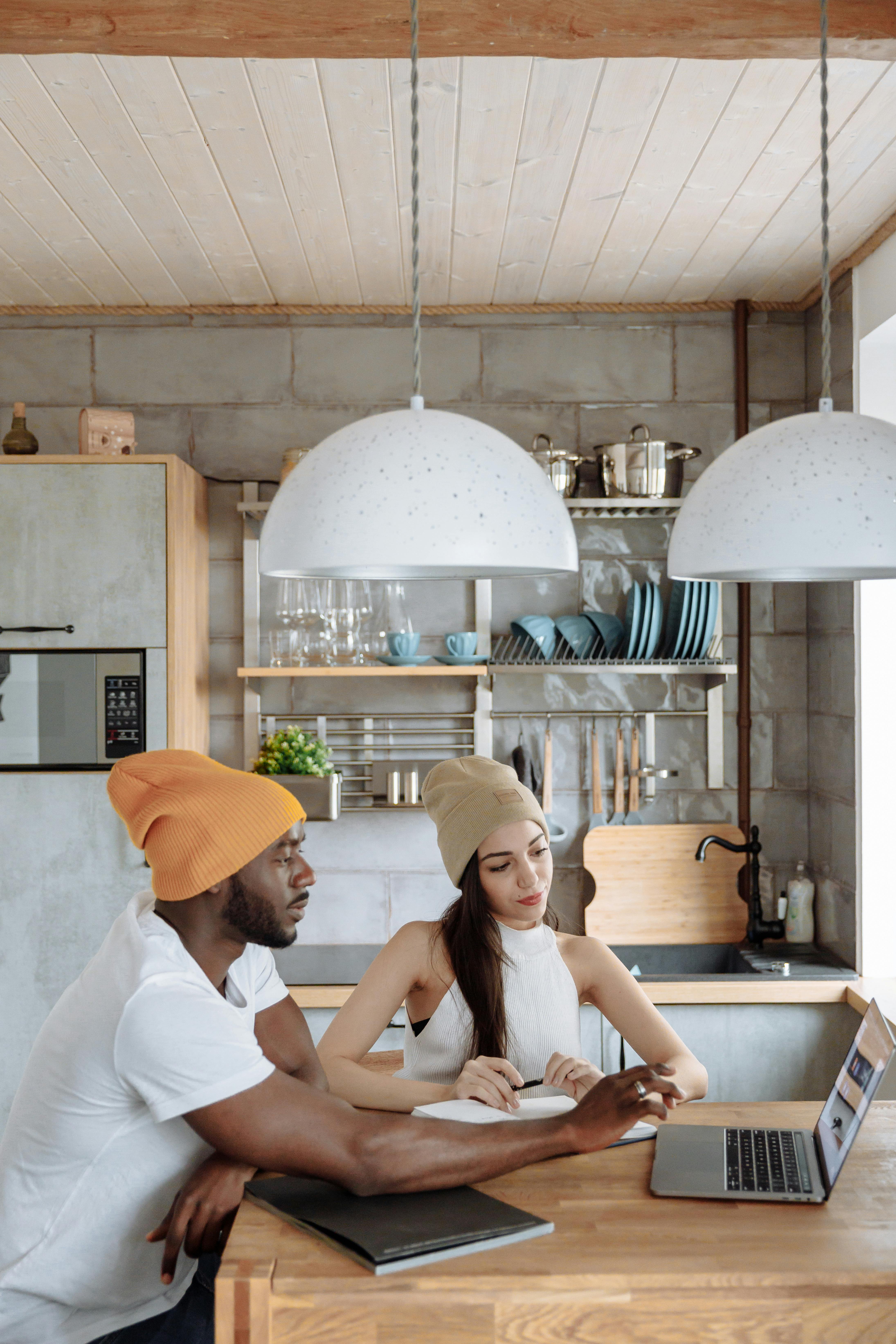 Two young adults working together on a laptop in a modern kitchen, representing teamwork and creativity.