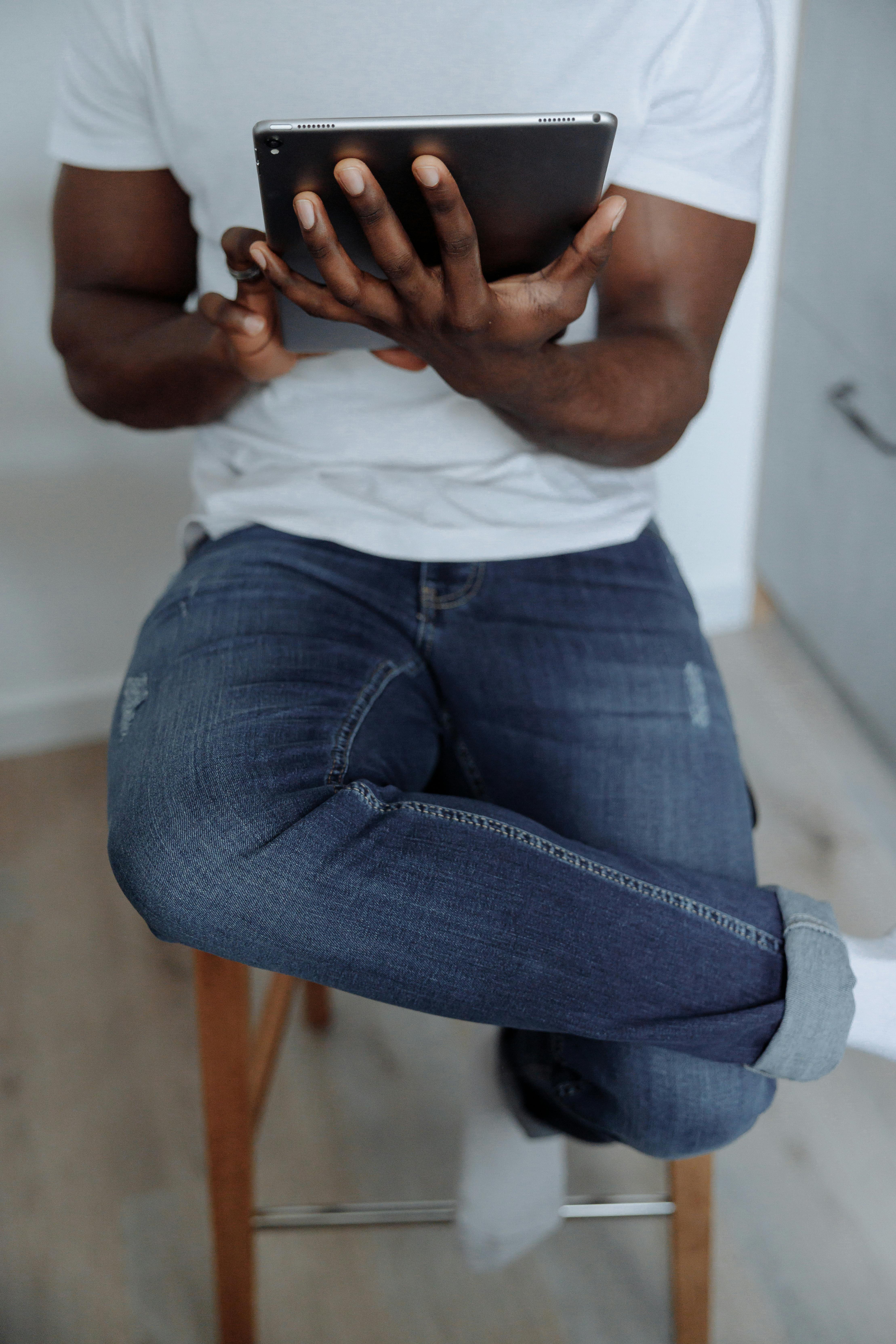 man in white tank top and blue denim jeans sitting on white concrete wall