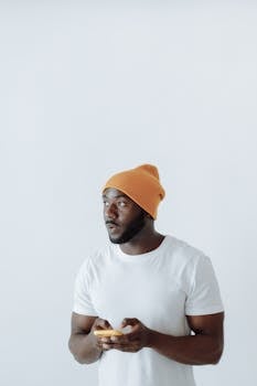 Portrait of a fashionable man in a white shirt and orange beanie, using a smartphone.