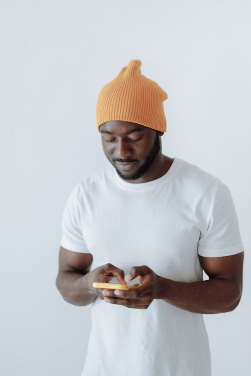  A Young Man in a Yellow Beanie Using a Smartphone