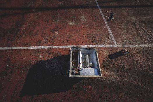 From above of outdoor lamp box placed on rough dirty ground of sports court on sunny day