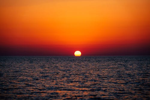 Picturesque scenery of bright sun in orange sky setting over endless waving ocean