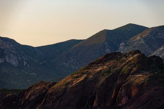 Breathtaking landscape of rocky mountains peaks and slopes against cloudless sunset sky in highlands