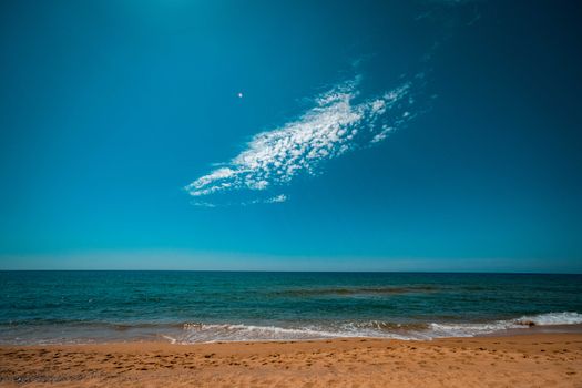 While stratus cloud in bright blue sky over endless waving sea washing sandy beach on sunny day
