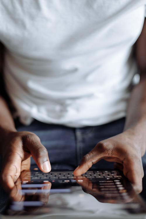 Person in White Shirt and Blue Denim Jeans Using Black Computer Keyboard