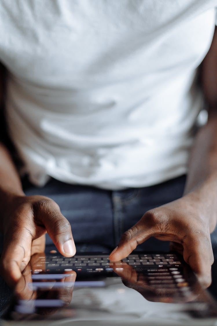 Person In White Shirt And Blue Denim Jeans Using Black Computer Keyboard