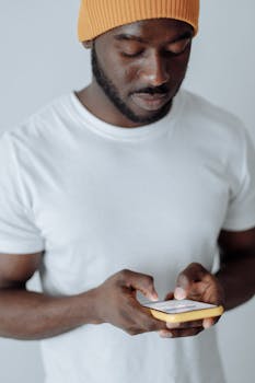 African American man wearing a beanie and white t-shirt using a smartphone in a studio setting.