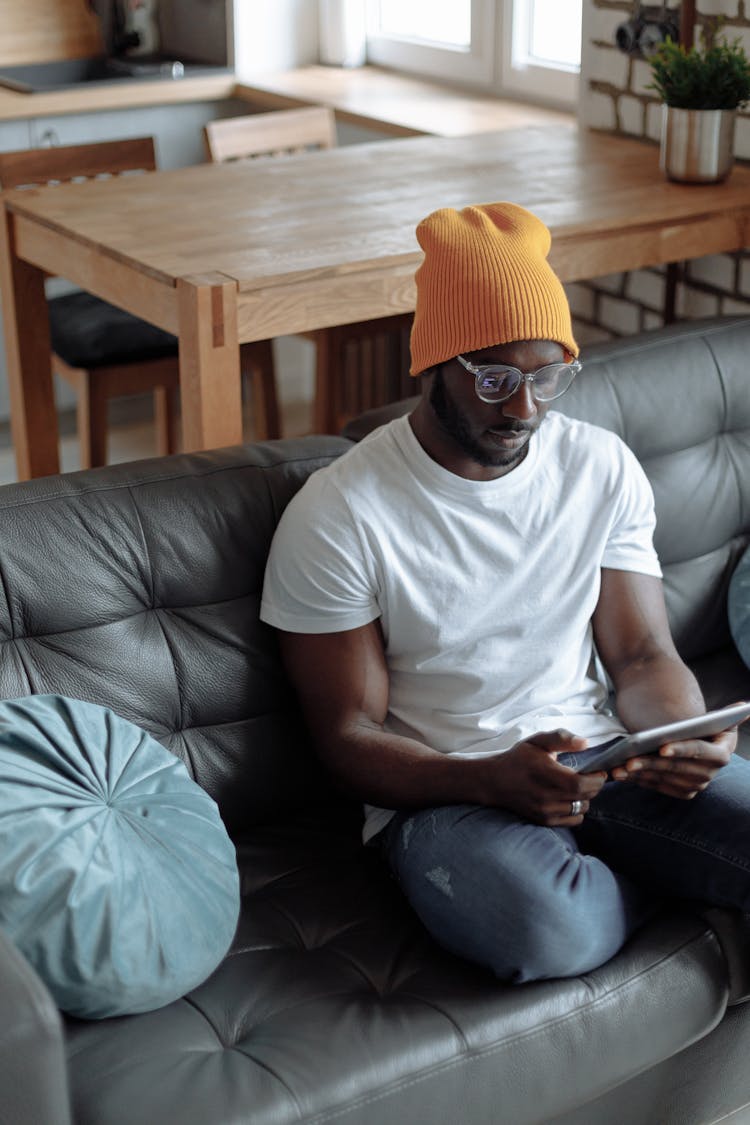 A Young Man In A Yellow Beanie Using A Tablet On A Couch