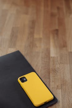 A yellow smartphone on a dark surface against a wooden background, offering ample copy space.