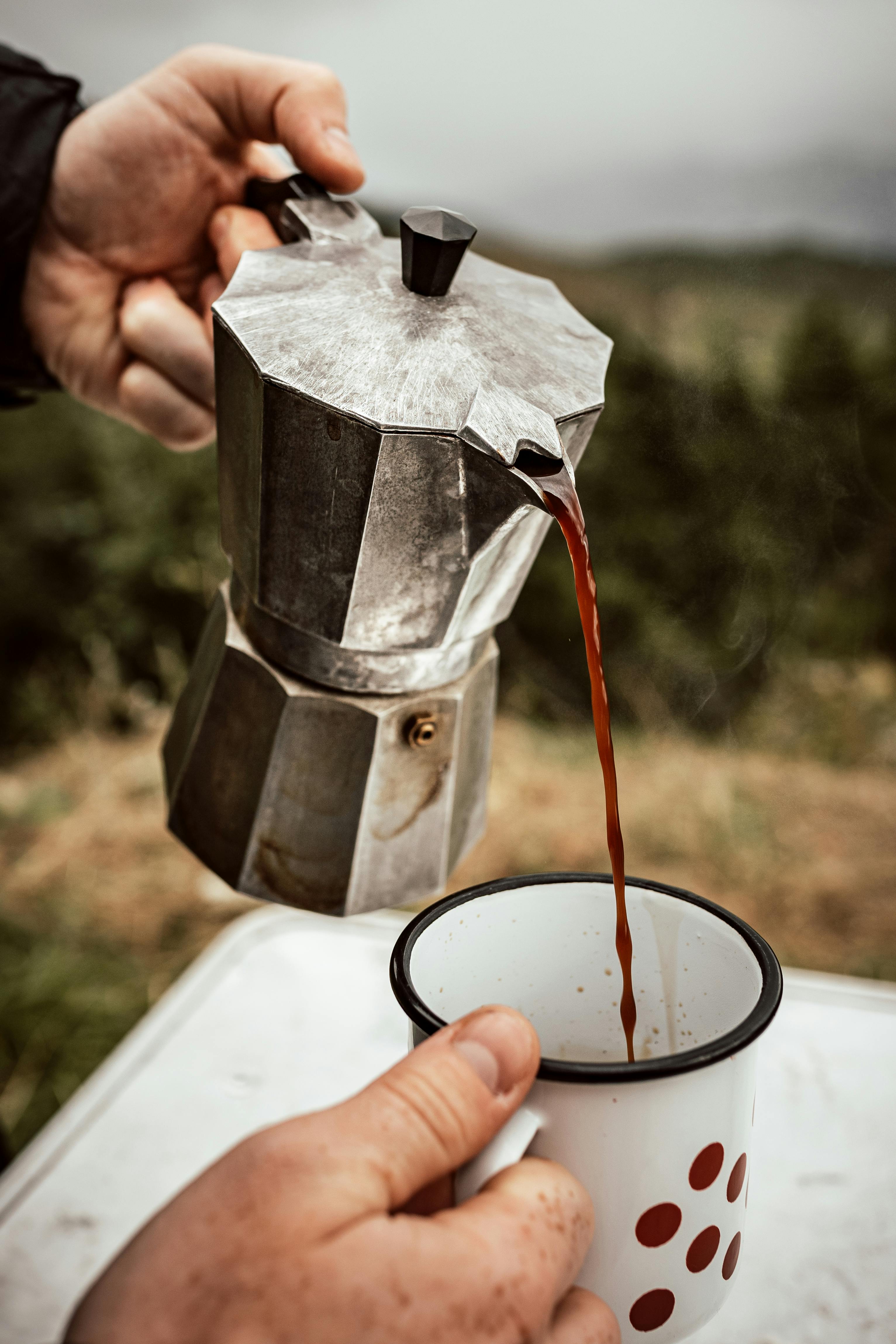 A rustic outdoor coffee pour from a vintage Moka pot into a polka dot mug, Italy.