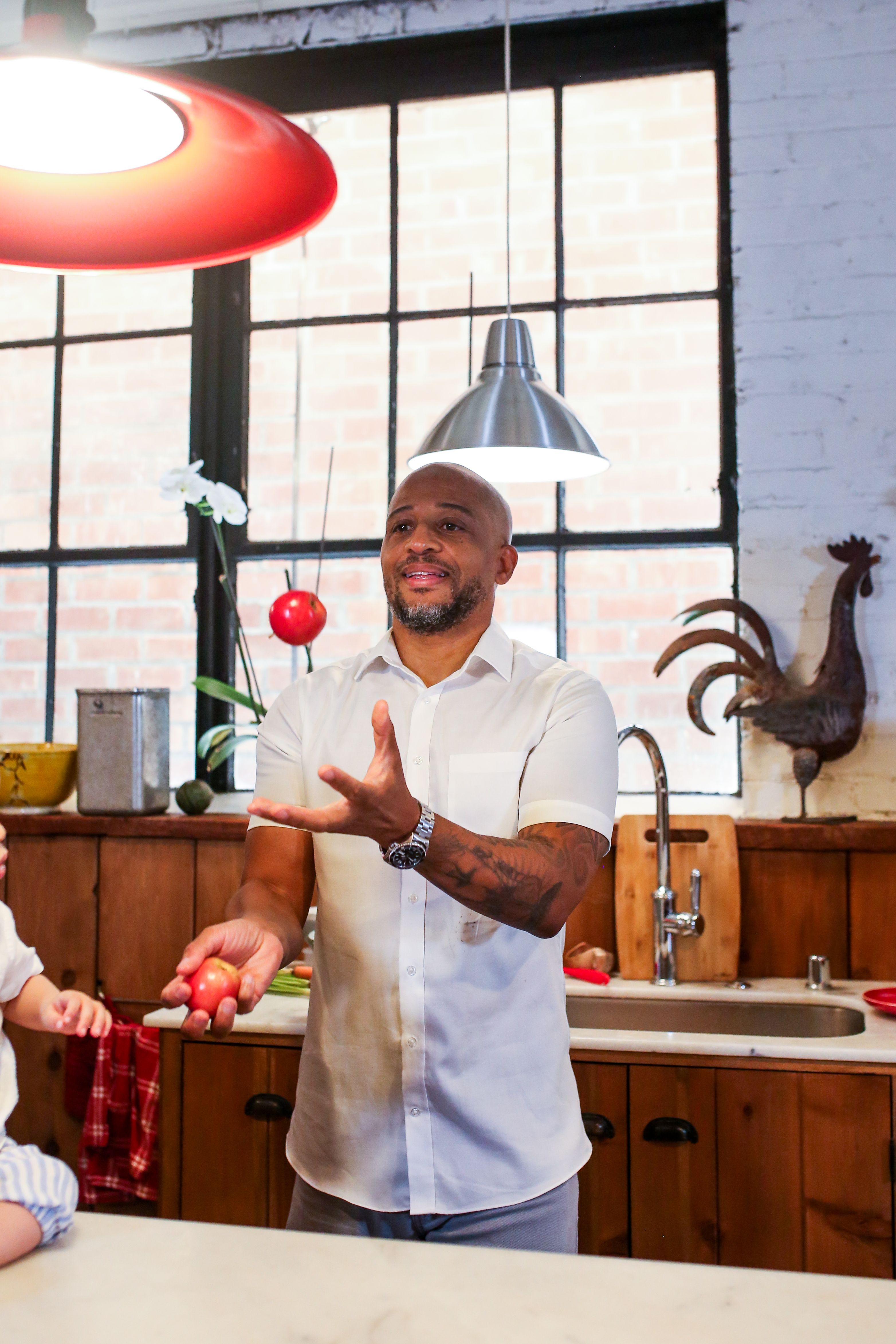 Smiling man juggling tomatoes in a rustic kitchen interior with vintage decor.