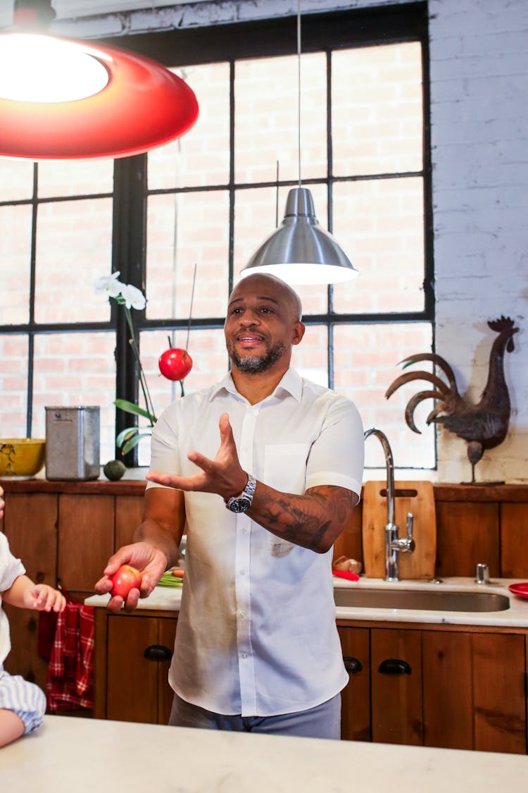 A Man Juggling Tomatoes In A Kitchen