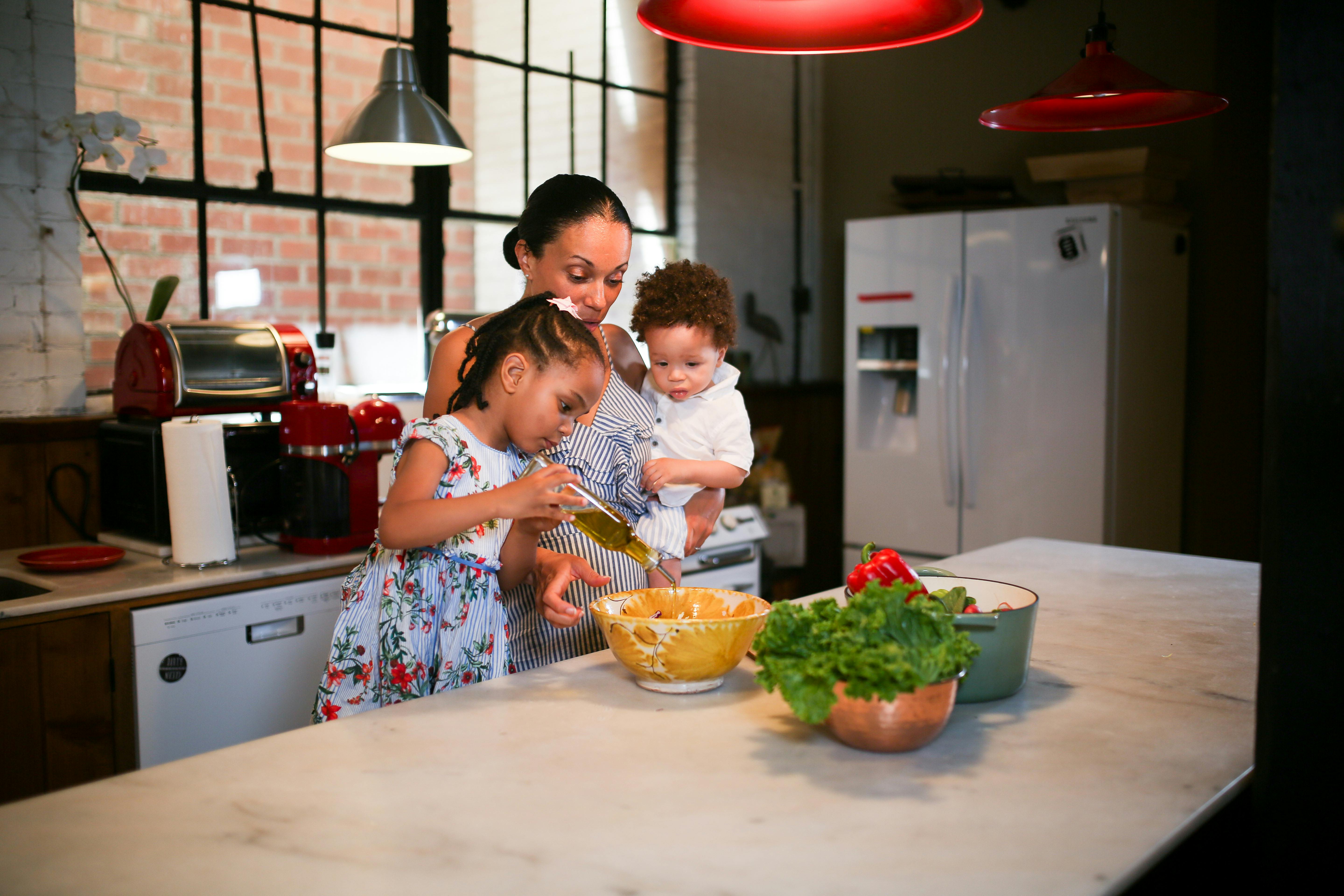 a little girl preparing food in a kitchen with her mom and brother