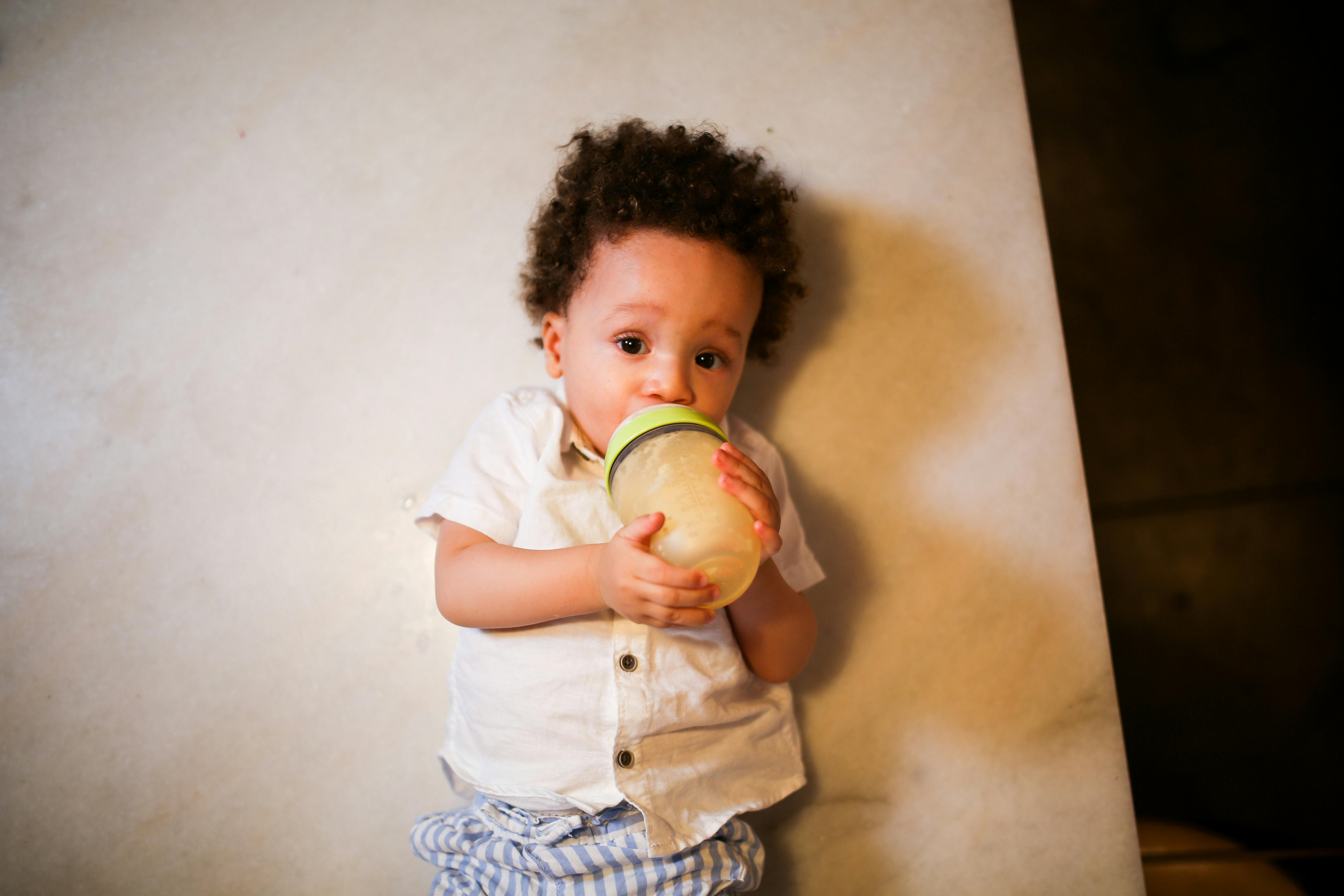 child in white shirt and blue and white shorts holding yellow and green apple