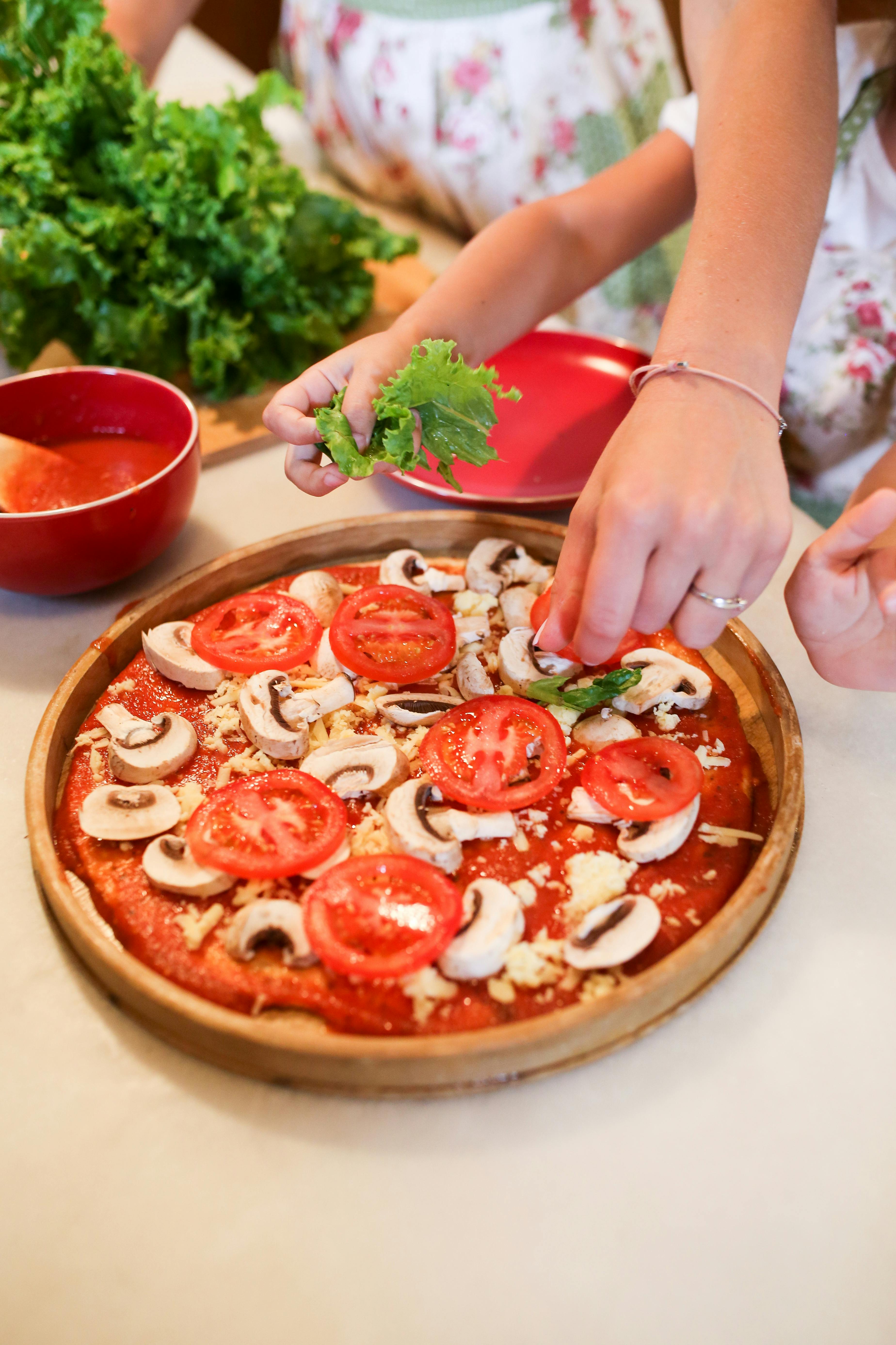 person holding pizza with tomato and basil on brown wooden round table