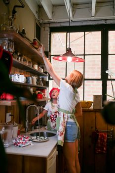 A mother helps her daughter reach for ingredients in a cozy kitchen, creating quality family time.
