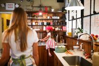 A young girl washing dishes while sitting on a kitchen counter in a cozy kitchen.