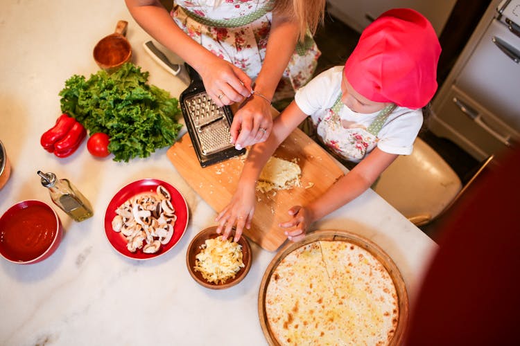 Mother And Daughter Preparing Pizza On Kitchen Counter Table