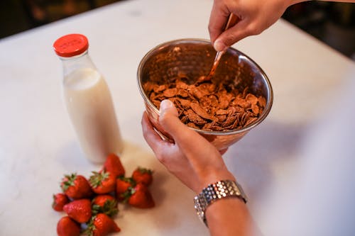 Person Mixing Chocolate Cereals on Stainless Bowl 