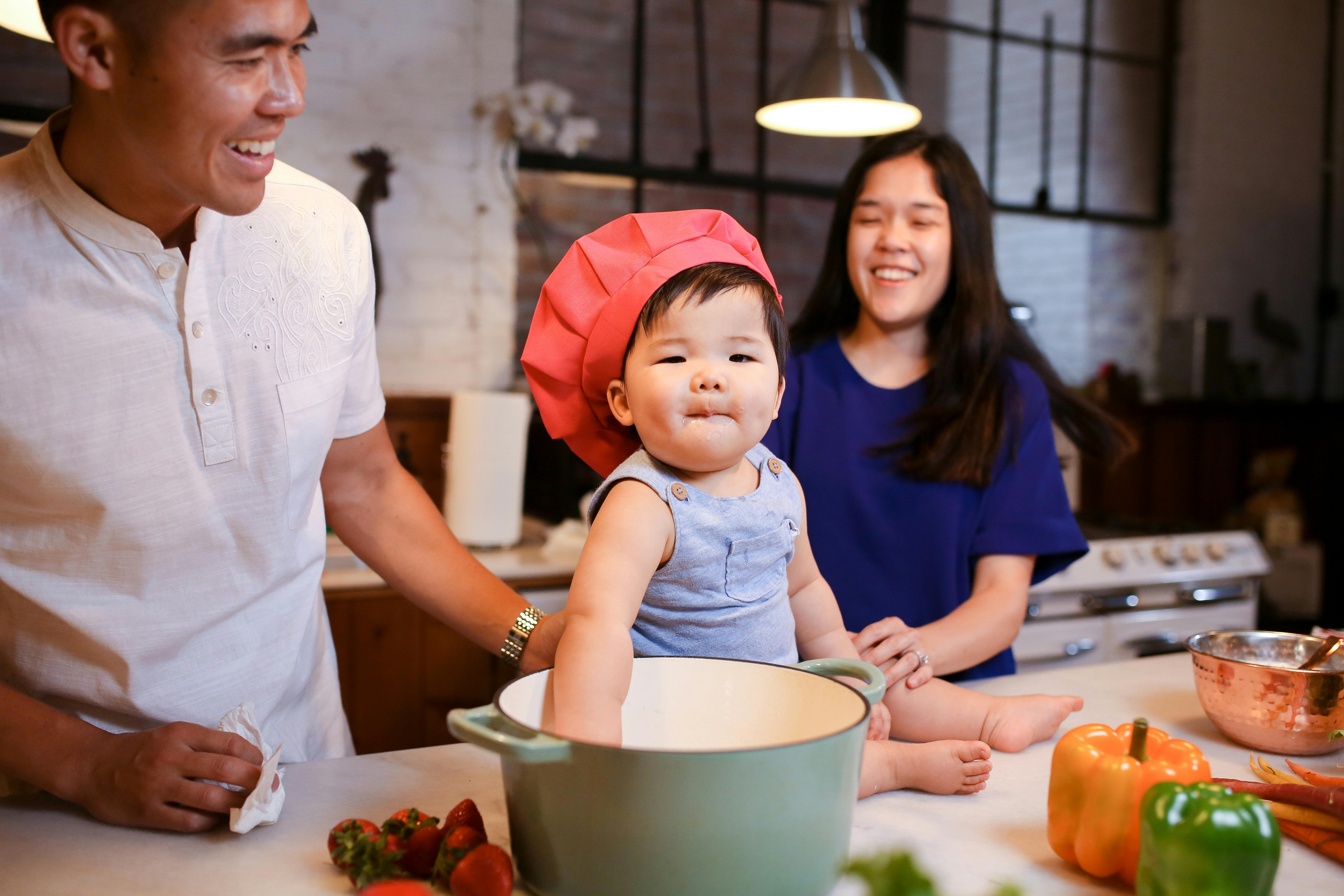 baby in red chef hat with her parents at her back