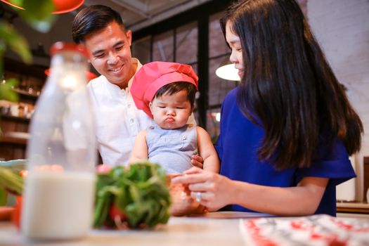 一家人带着一个戴着厨师帽的幼儿在室内做饭