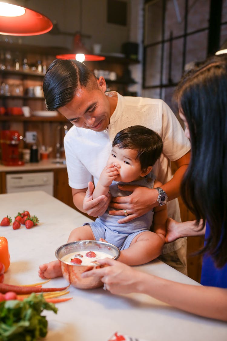 A Man Feeding A Baby Sitting On A Kitchen Counter