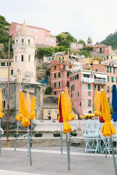 Cityscape with bright modern buildings on hillside and pavement with colorful umbrellas under clear sky