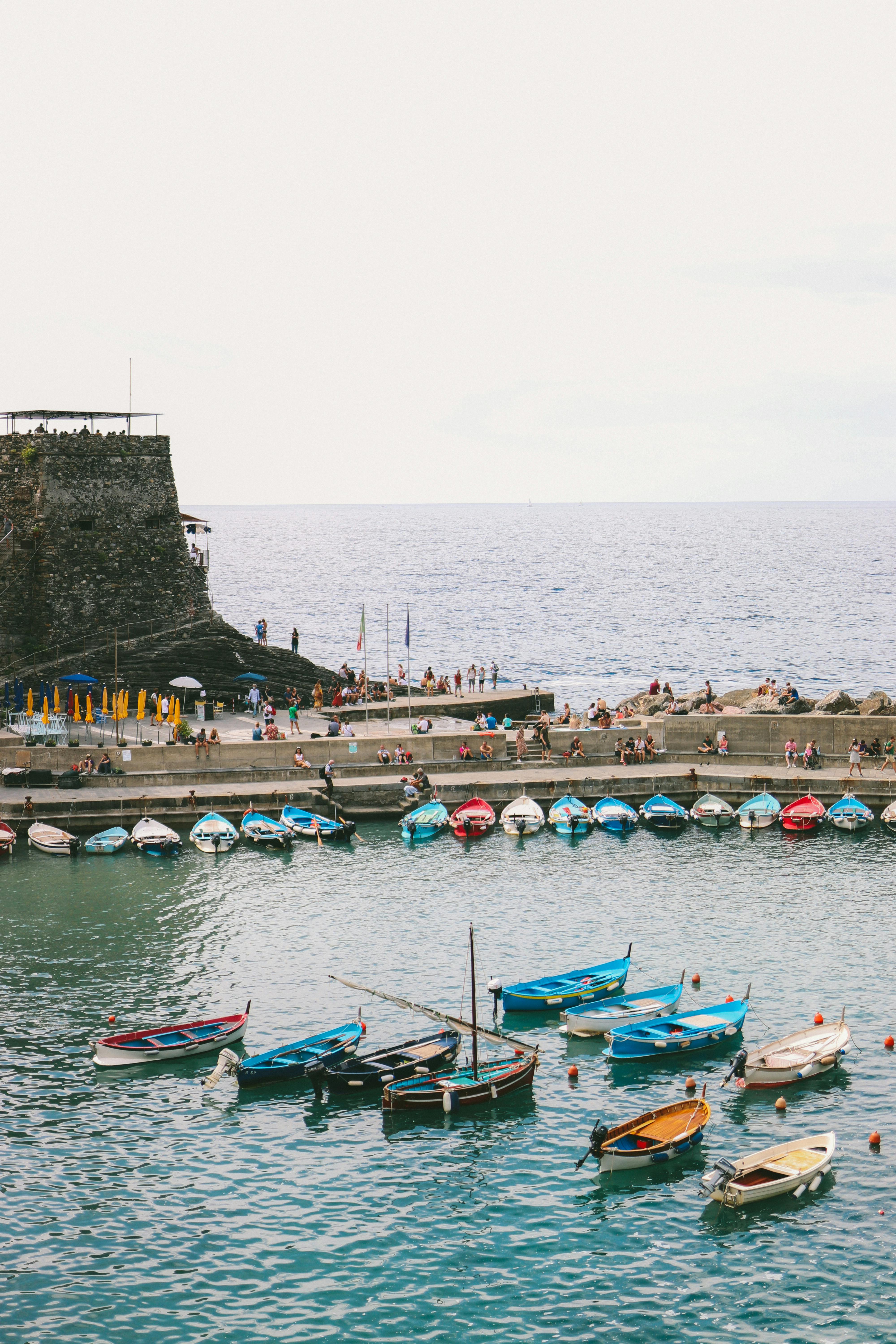 Peaceful seaside harbor with colorful boats near a rugged cliff under a serene sky.