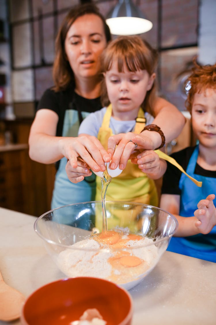 A Parent Cracking An Egg Into A Mixing Bowl With Her Child