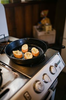 Slices of baguette with herbs cooking in a cast iron skillet on a stove.