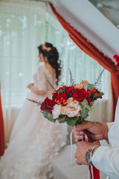 Bride standing with bouquet in luxurious white wedding dress indoors.